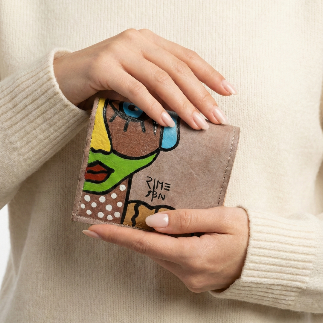 Hand-painted beige leather wallet with cubist abstract portrait, green cheek, and white polka dots. Signed by Rime Sbai.